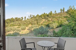 A balcony with two wicker chairs and a small round table, overlooking a hillside with various trees and shrubs. - Orama 20 Room with Sea View, Wi-Fi, and Air Conditioning (Εύβοια)