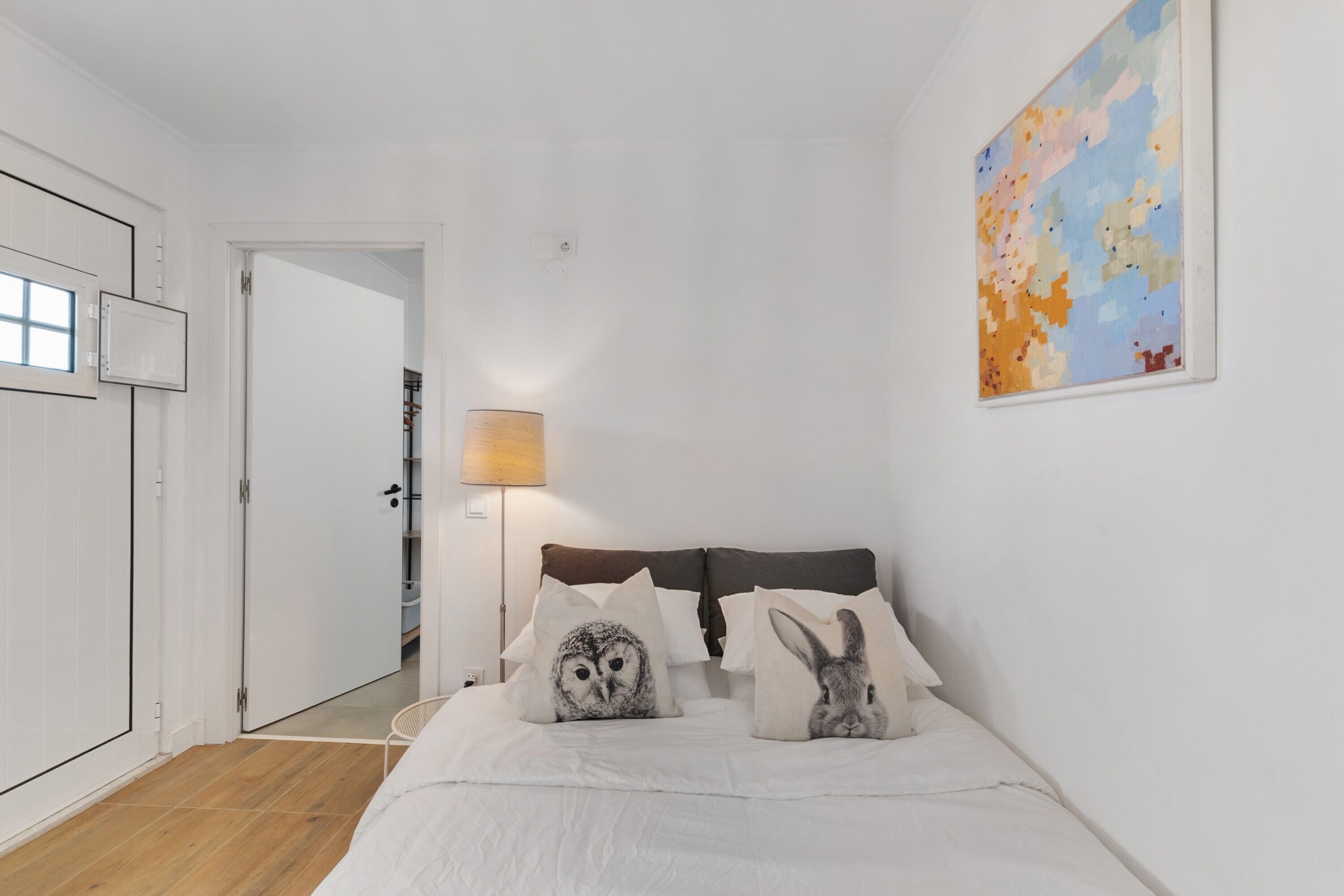 A bedroom with a bed, a nightstand, a lamp, and a wall-mounted painting.