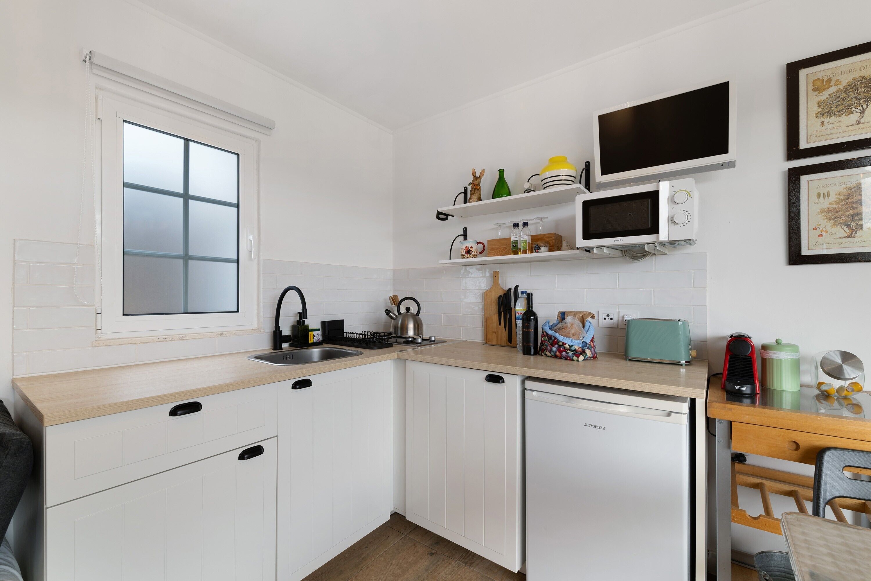 A compact kitchen with white cabinetry, a window, a microwave, a toaster, and a sink.