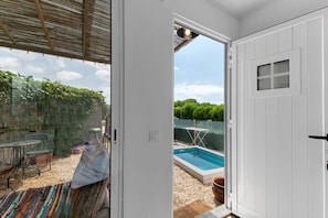 Habitació amb porta corredissa de vidre que dona a zona exterior amb piscina, zona de seients coberta i vista a un paisatge verd.