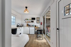 Een compacte, moderne keuken met een eethoek, een bed en een grote schuifdeur naar een balkon.