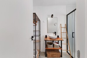 Een moderne badkamer met een wit wastafelmeubel, een spiegel en een houten trap.
