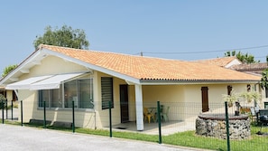 Ein eingeschossiges Haus mit Ziegeldach, einer Veranda und einem eingezäunten Garten.