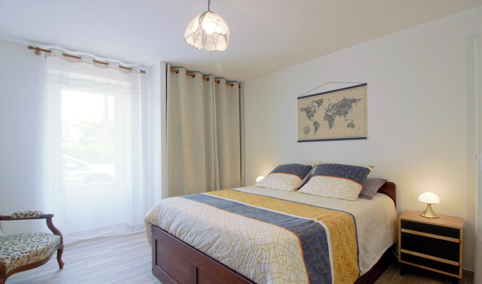 A bedroom with a bed, a chair, a nightstand, a lamp, and a world map on the wall.