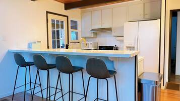 Cozinha moderna com ilha central, banquetas e um lixo de aço inoxidável.