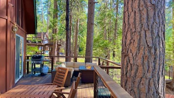 A wooden deck with outdoor furniture, a grill, and a view of tall trees.