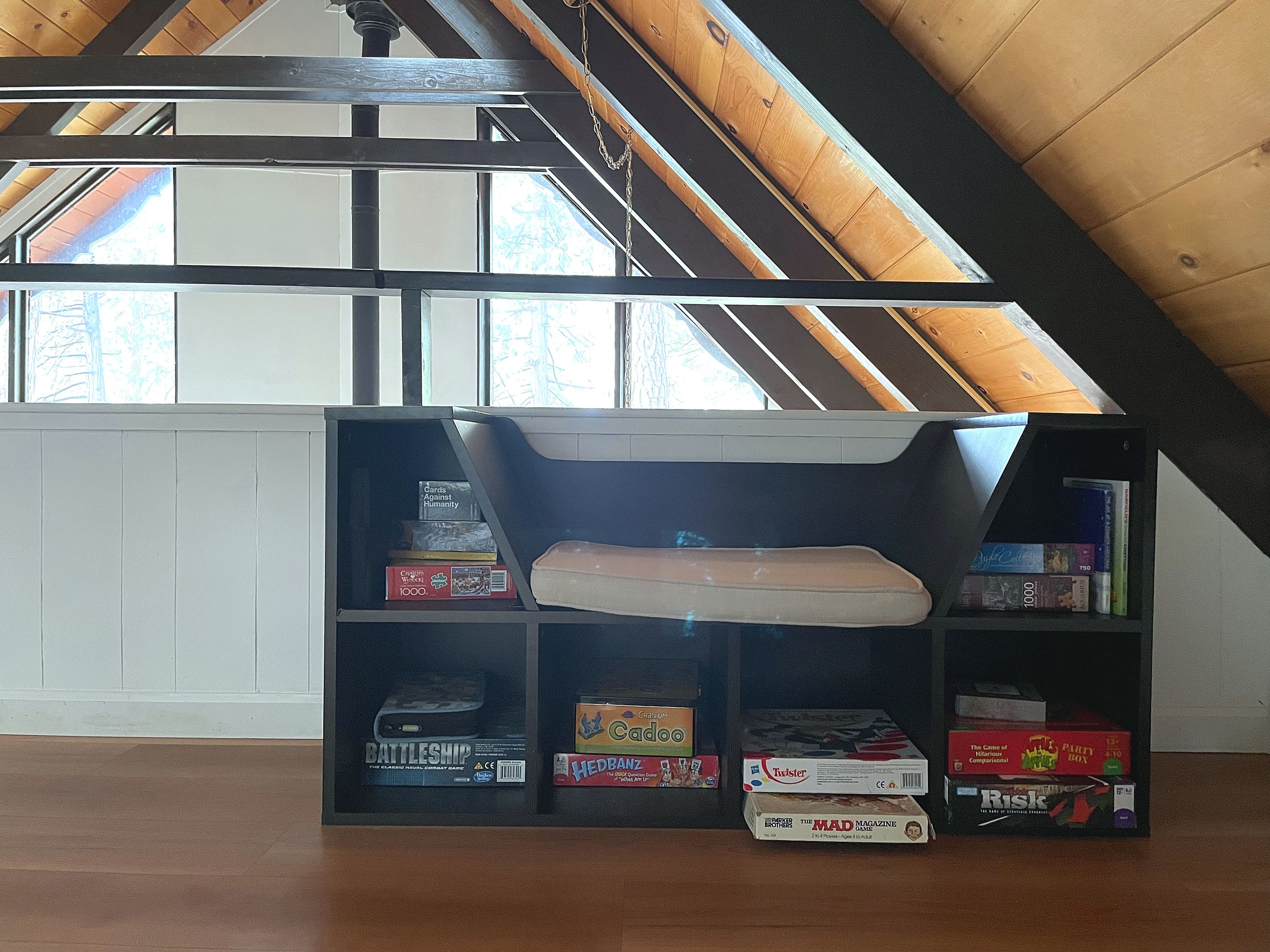 Ein Loft-Zimmer mit schrägem Dach, einer eingebauten Bücherwand und einer gepolsterten Sitzbank.