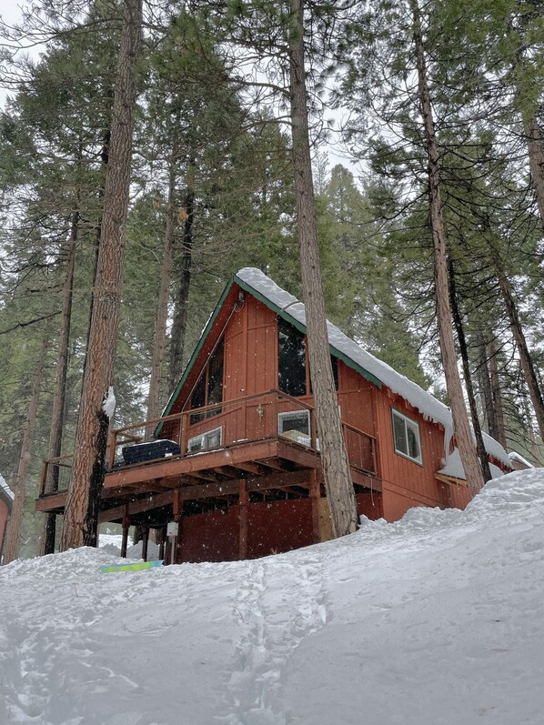 A cabin with a balcony, surrounded by tall pine trees and covered in snow.