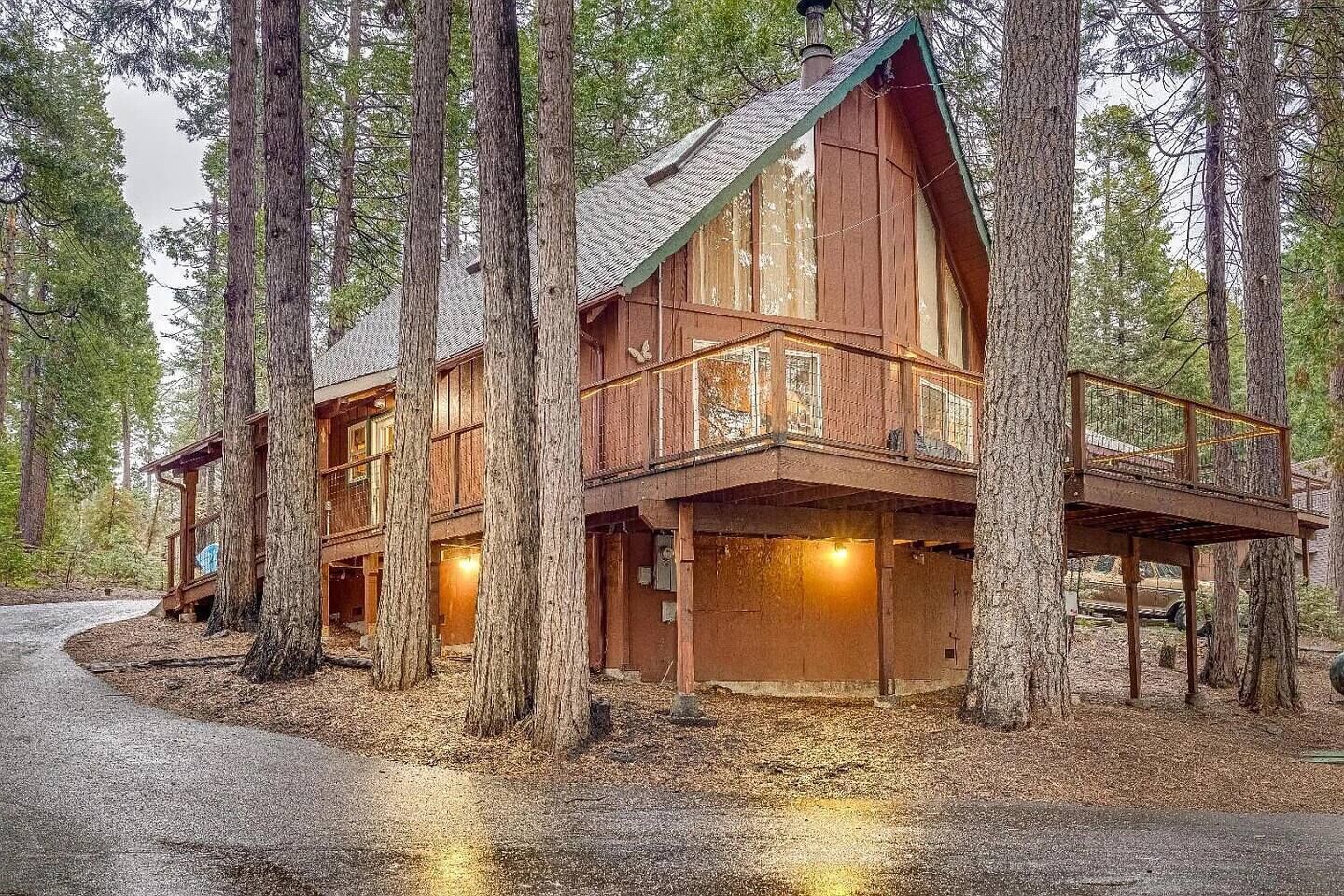 A wooden cabin with a balcony, surrounded by tall trees.