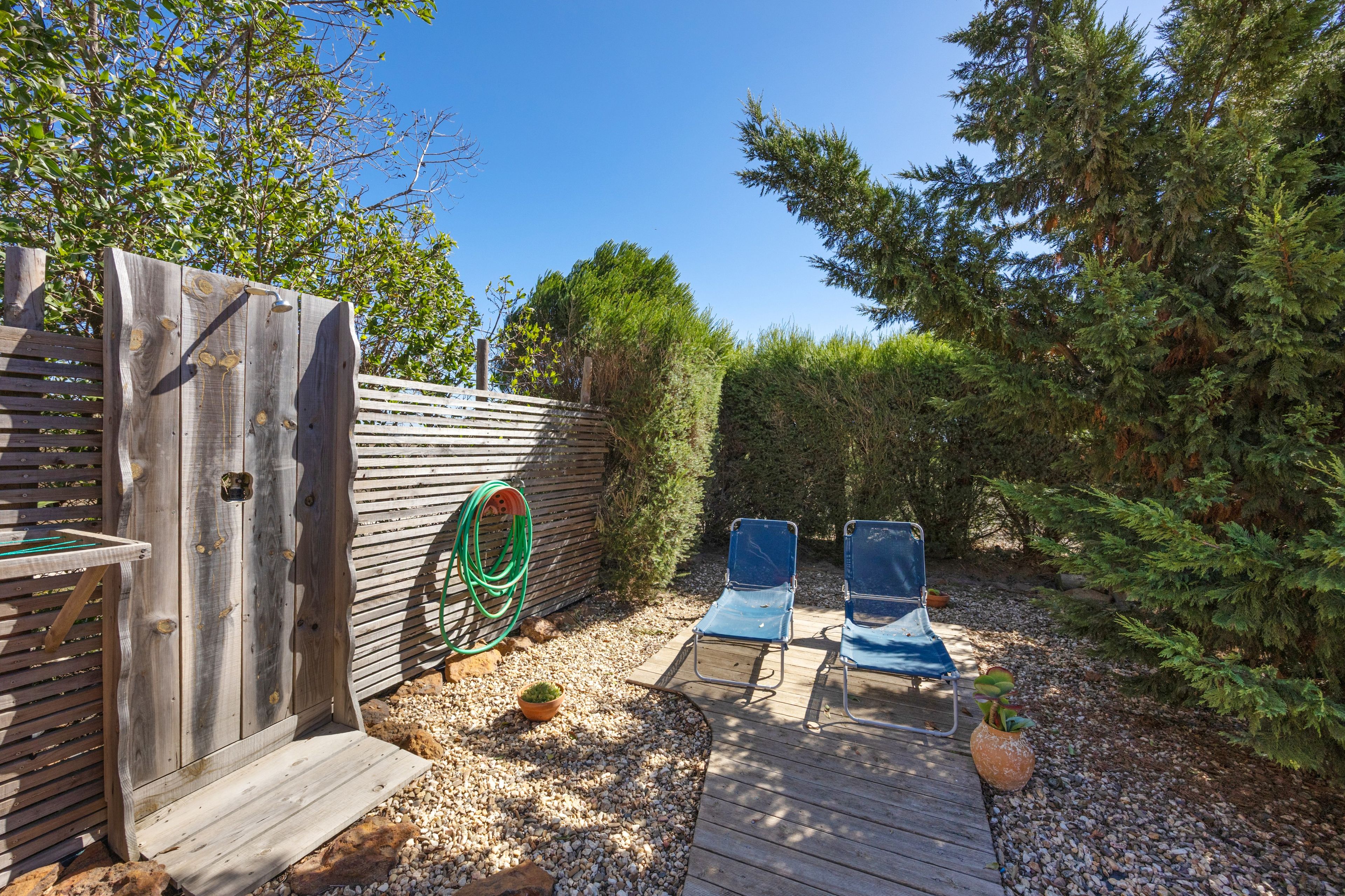 A wooden deck with two blue chairs, a hose, and a wooden fence with a metal gate.