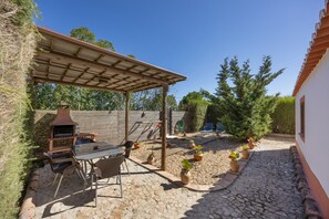 Un patio techado al aire libre con una parrilla, asientos y plantas en macetas.