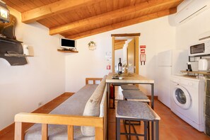 Cocina compacta con lavadora, microondas y un pequeño comedor con banco.