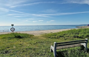 Eine Bank mit Blick auf einen Strand, bewölkter Himmel und ruhiges Meer.