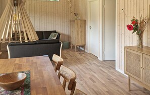 Ein Holzinterieur mit einer Couch, einem Esstisch, Stühlen, einem Schrank und einer Pendelleuchte.