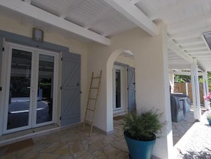 A covered patio area with a stone floor, a blue potted plant, and a wooden ladder leaning against a wall. - La Dune Blanche Vacation Rental - GUJAN MESTRAS (GUJAN MESTRAS)