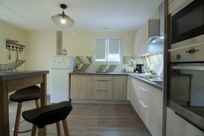 A compact kitchen with a built-in oven, a microwave, and a sink. There is a small dining area with two stools. - La Dune Blanche Vacation Rental - GUJAN MESTRAS (GUJAN MESTRAS)