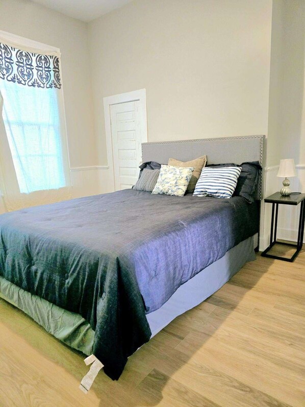 A bedroom with a bed, pillows, a bedside table, and a window with curtains.