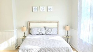A bedroom with a bed, two bedside tables, and three framed artworks on the wall.