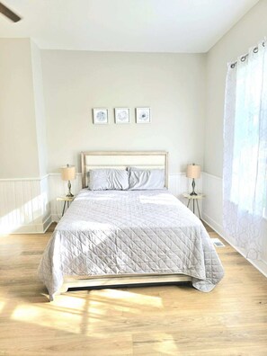 A bedroom with a bed, two bedside tables, and three framed artworks on the wall.