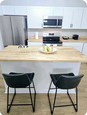 A kitchen with a central island, two black chairs, a stainless steel refrigerator, a microwave, and a stove.