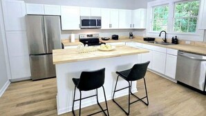 A modern kitchen with white cabinets, a stainless steel refrigerator, a microwave, and a wooden island with two black bar stools.