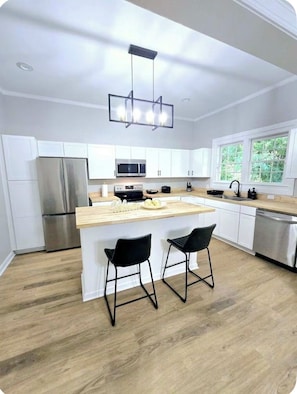 A modern kitchen with white cabinets, a stainless steel refrigerator, a microwave, and a wooden island with two black bar stools.