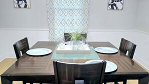A dining room with a rectangular table, four chairs, a chandelier, and two abstract paintings on the walls.