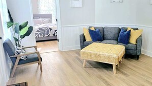 A living room with a sofa, a coffee table, a chair, and a bed in the background.