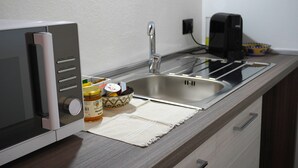 Una cocina con microondas, un lavamanos y una cafetera. Hay frascos de mermelada y una botella de agua en la encimera.