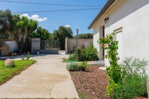 Propiedad residencial con camino de entrada pavimentado, acceso por portón y área de jardín con diversas plantas y arbustos.