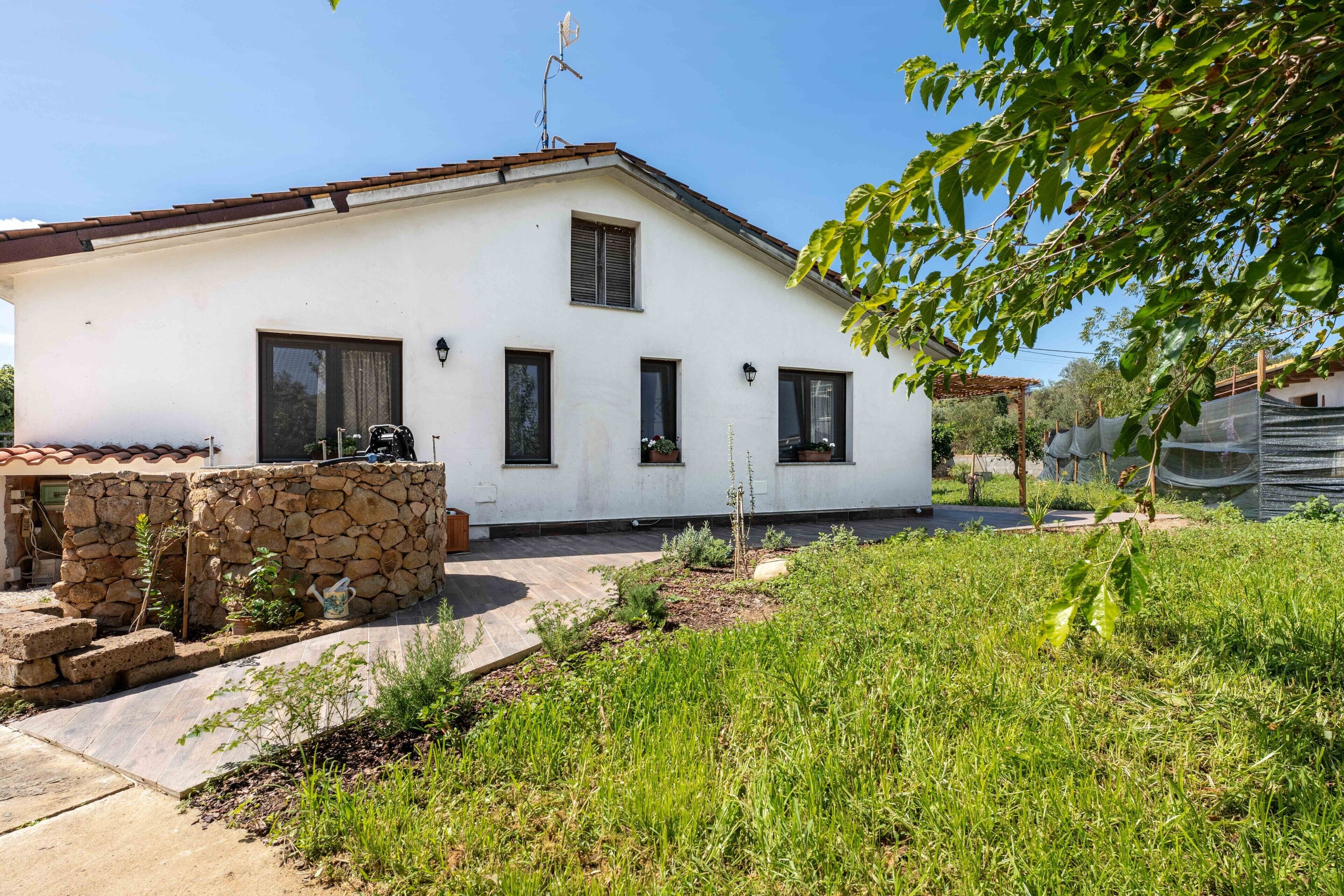 A white building with a stone wall, windows, and a garden.