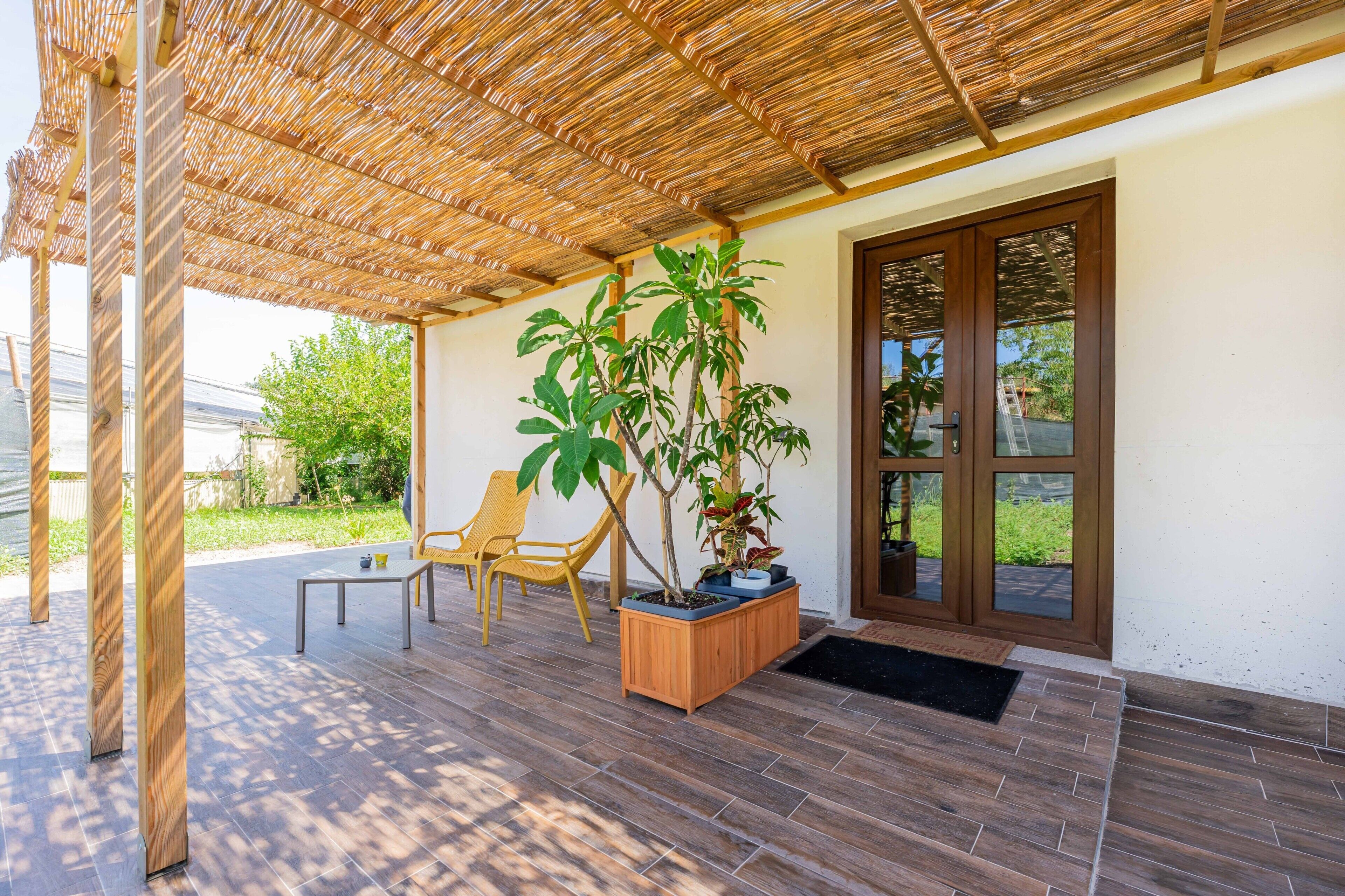 A covered patio area with wooden flooring, a table, chairs, and potted plants.