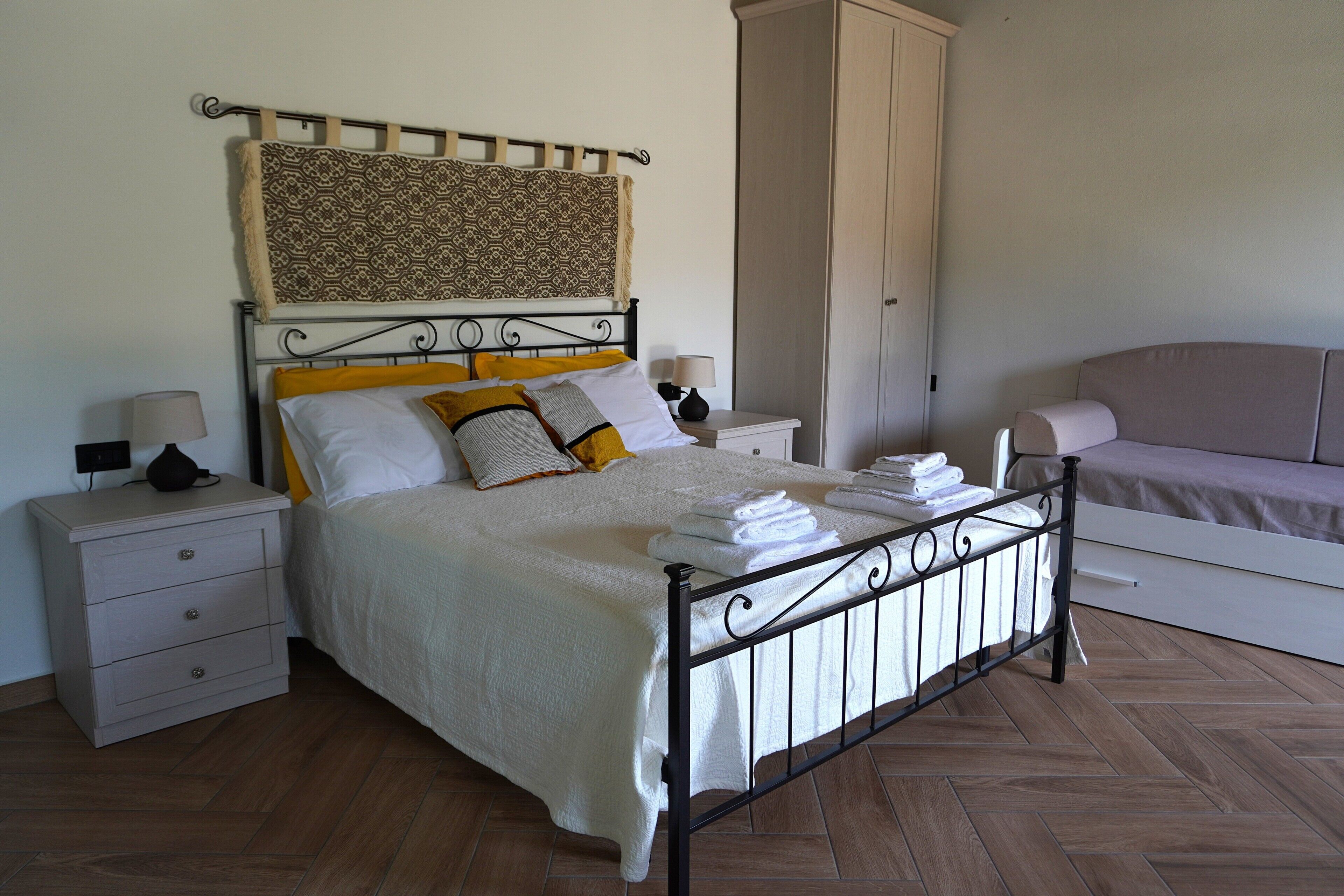 Un lit bien fait, avec du linge de lit blanc, une table de chevet avec une lampe et une armoire dans une chambre.