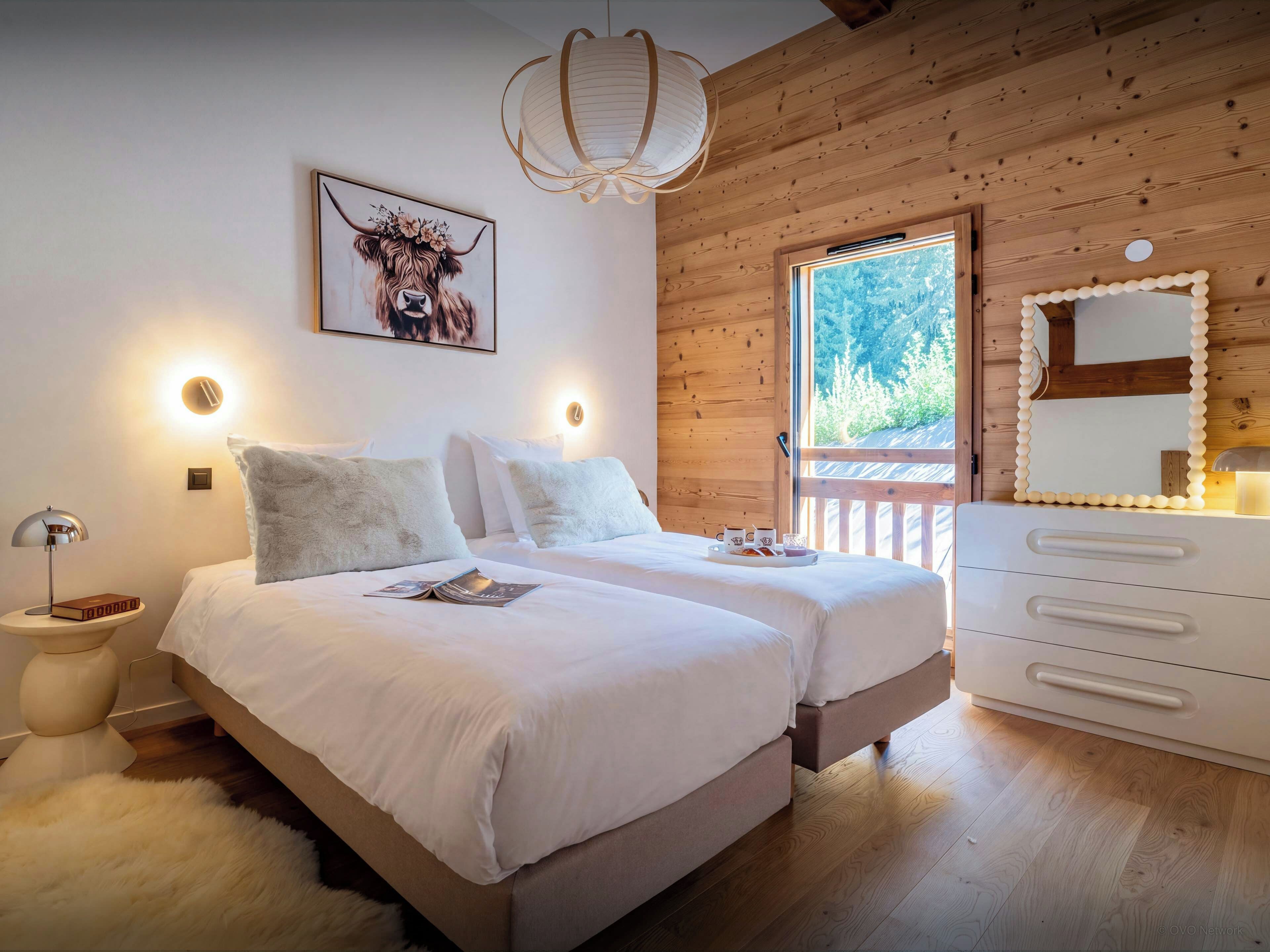 A bedroom with two beds, a wooden ceiling, a large window, and a mirror with a decorative frame.