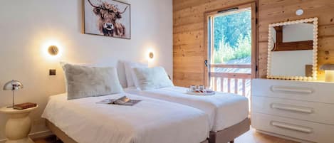 Ein Schlafzimmer mit zwei Betten, einer Holzbalkendecke, einem großen Fenster und einem Spiegel mit dekorativem Rahmen.