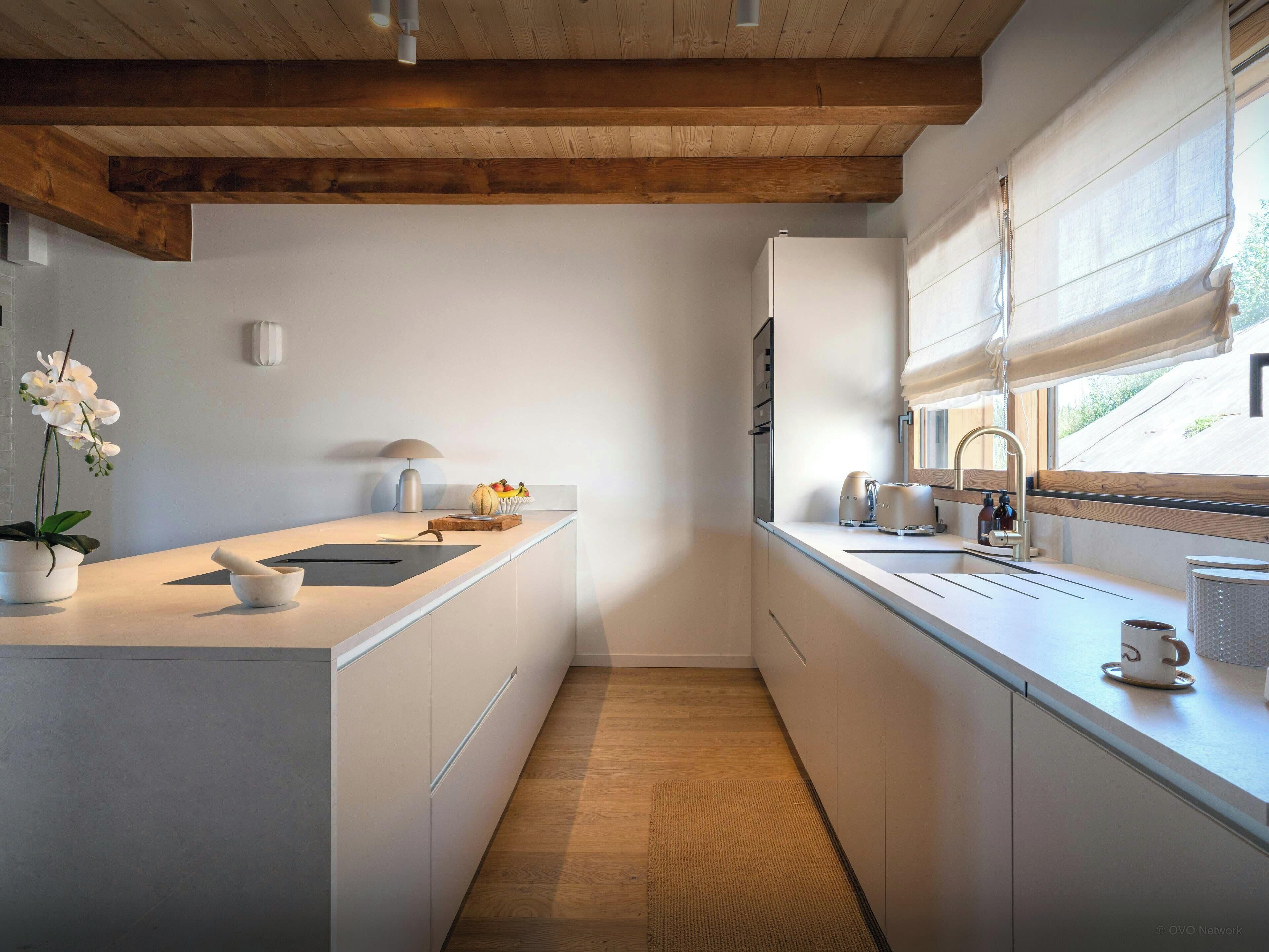 Una cocina moderna con techo de madera, armarios blancos y un ventanal grande.