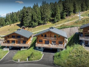 Une cabane en bois dotée d’un balcon, entourée d’une zone boisée et avec une montagne en arrière-plan.