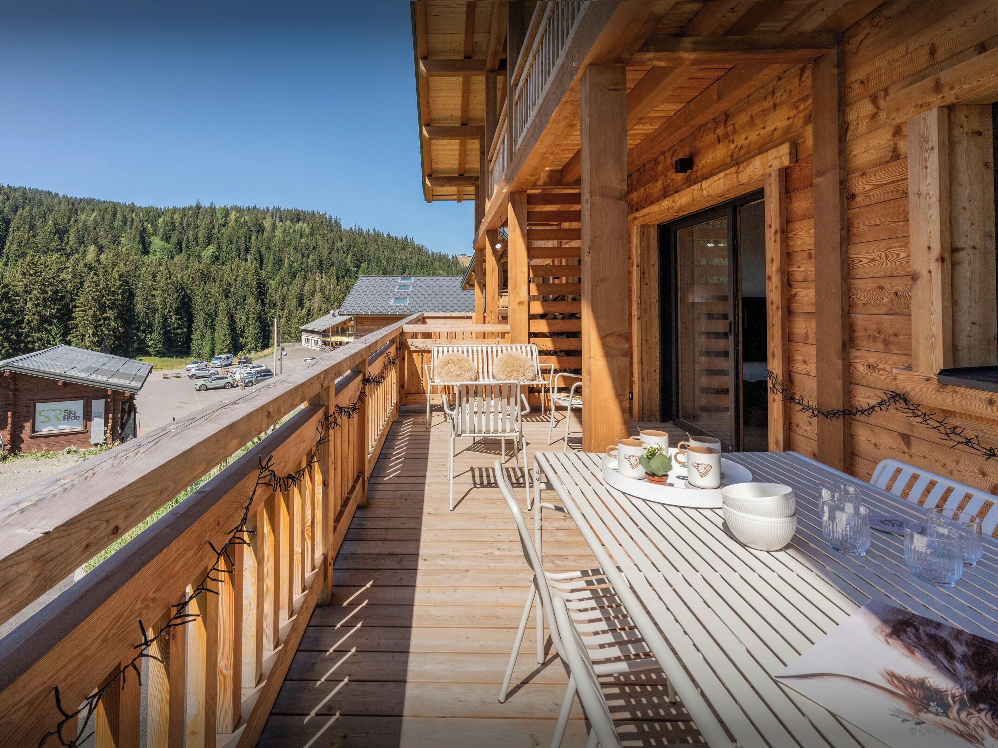Un balcon en bois avec une table et des chaises, donnant sur une zone boisée.