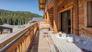 En træterrasse med bord og stole, med udsigt over et skovområde.