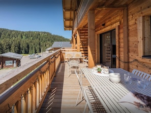 Un balcon en bois avec une table et des chaises, donnant sur une zone boisée.