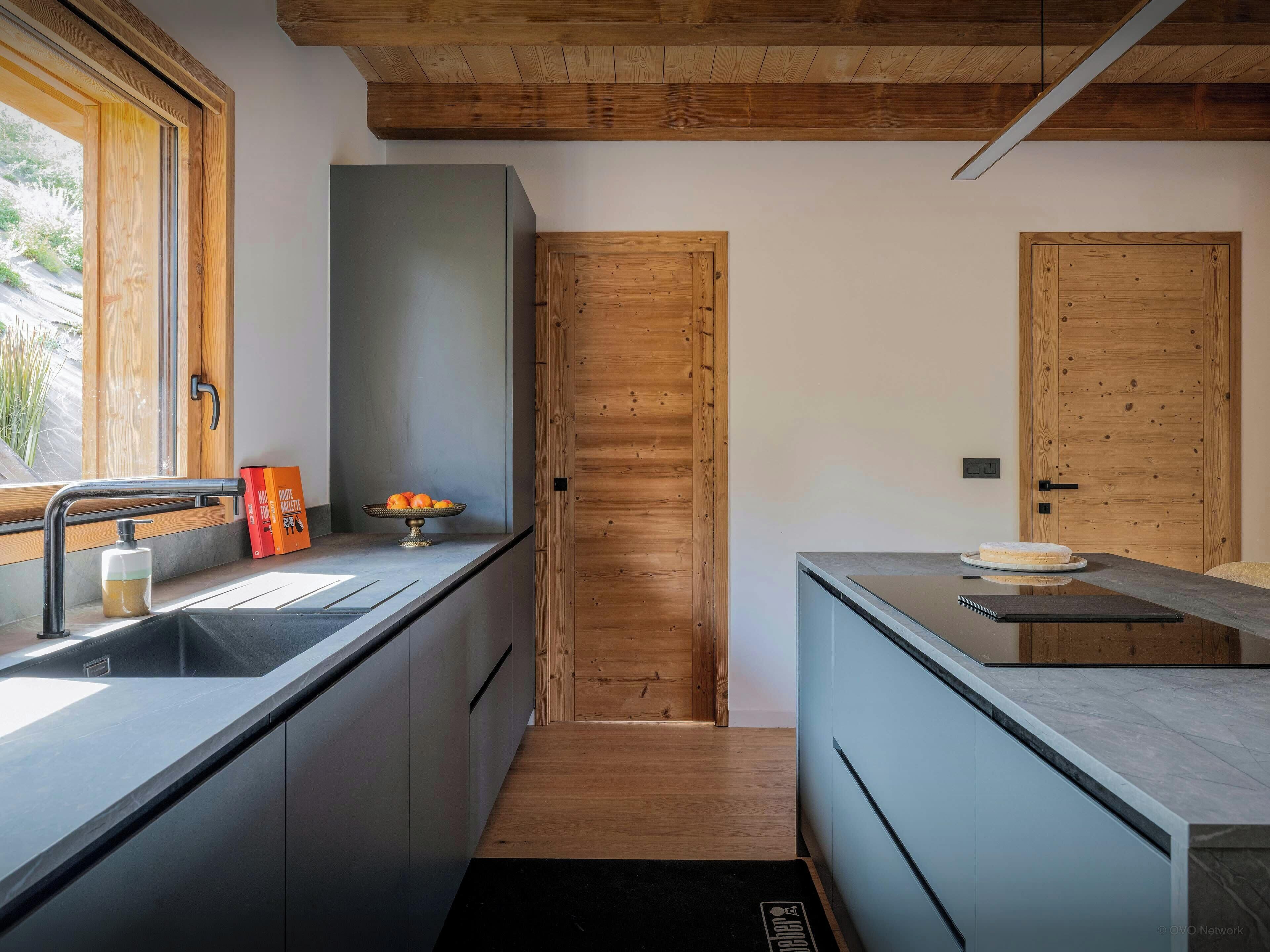 Una cocina moderna con puerta de madera, un lavamanos con dispensador de jabón y un cuenco de fruta sobre la encimera.