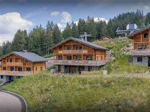Une cabane en bois dotée d’un balcon, entourée d’une colline boisée.