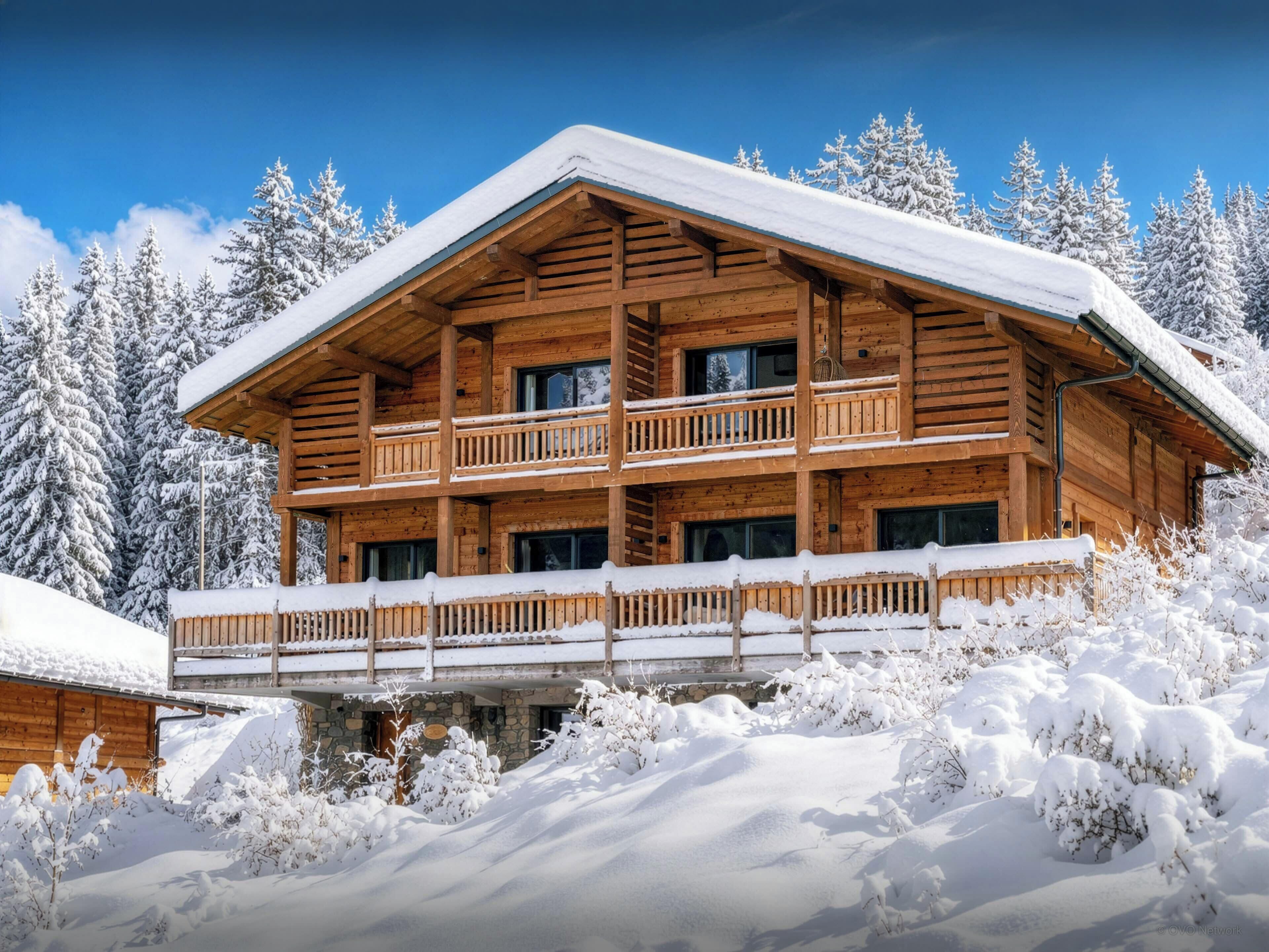 Una cabaña de madera de varios pisos con balcones, rodeada de árboles cubiertos de nieve.