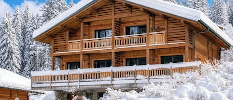 Un chalet en bois à plusieurs étages, doté de balcons et entouré d’arbres couverts de neige.