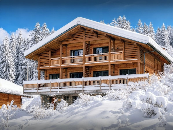 A multi-story wooden chalet with balconies, surrounded by snow-covered trees.