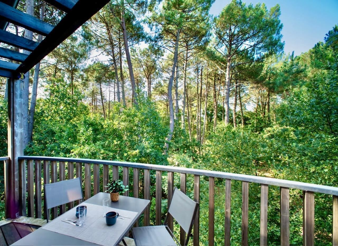 A wooden deck with a table and chairs, overlooking a forested area.