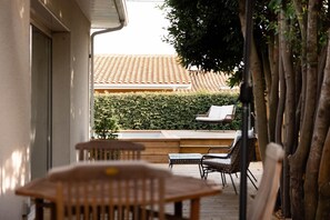 Een terras met tuinmeubilair, een haag en een pannendak op de achtergrond.