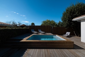 Een rechthoekig zwembad met een houten terras, twee ligbedden en een houten omheining.