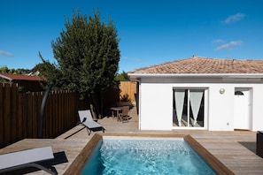 A swimming pool with a wooden deck, a small white building with a tiled roof, and a wooden fence. - L'Echappée du Bassin - ARES (ARES)