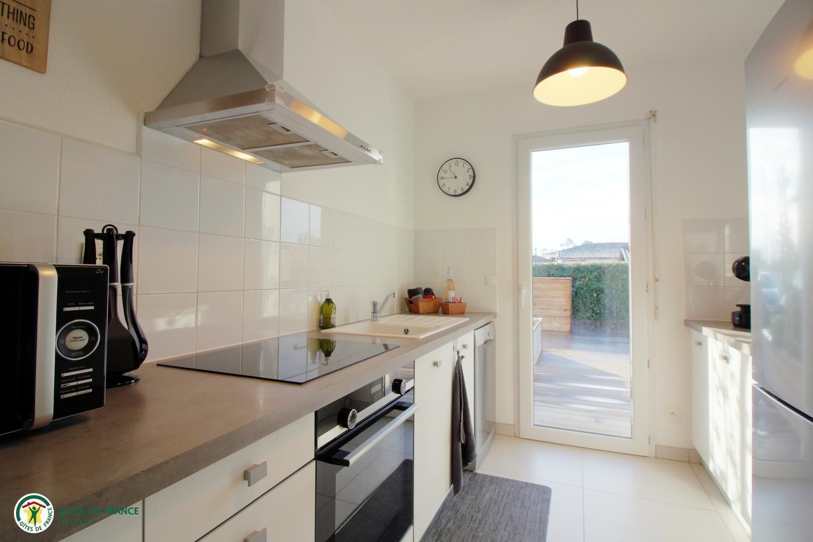 A modern kitchen with a built-in oven, a range hood, a sink, and a clock on the wall.